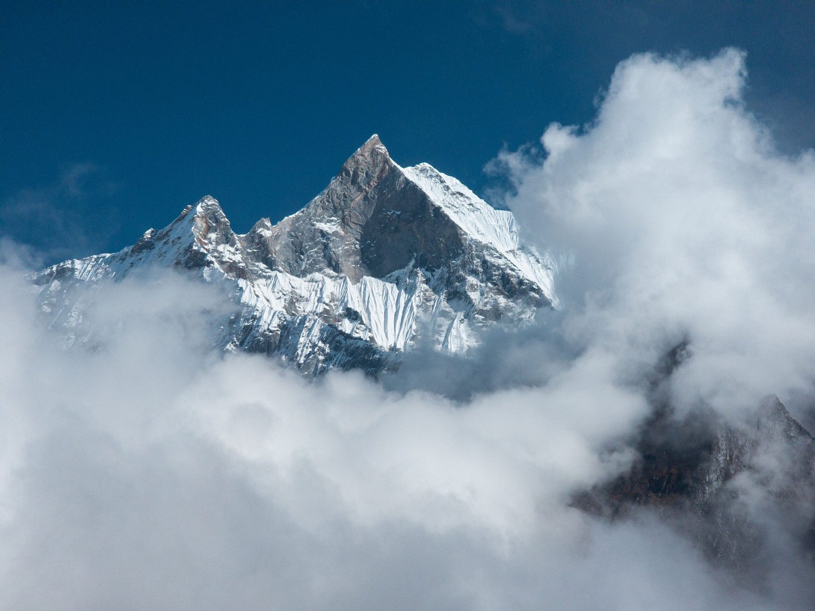 Snow-covered Himalayan peak piercing through clouds under a blue sky.